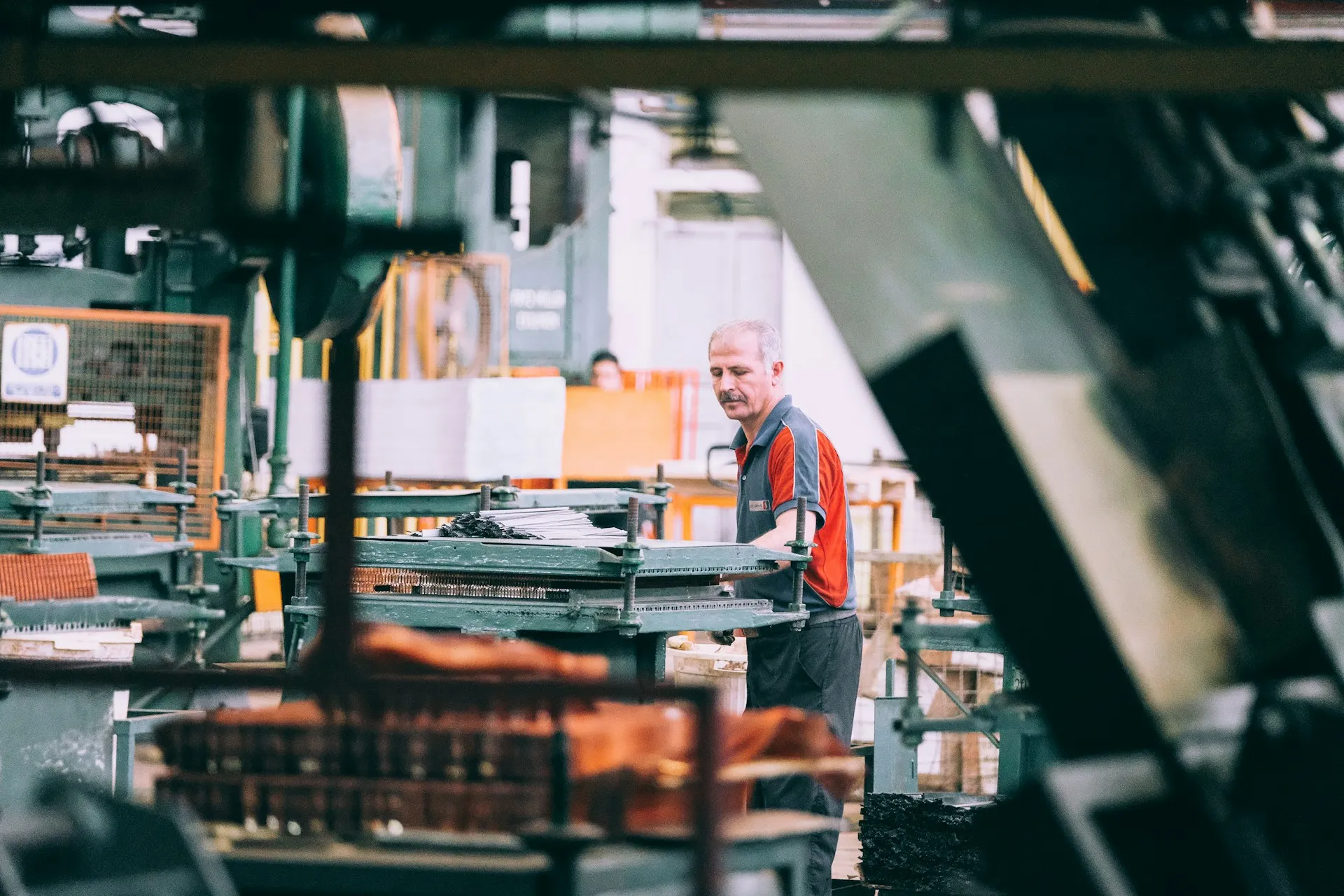 A worker loading sheet metal parts into a press machine on a factory floor