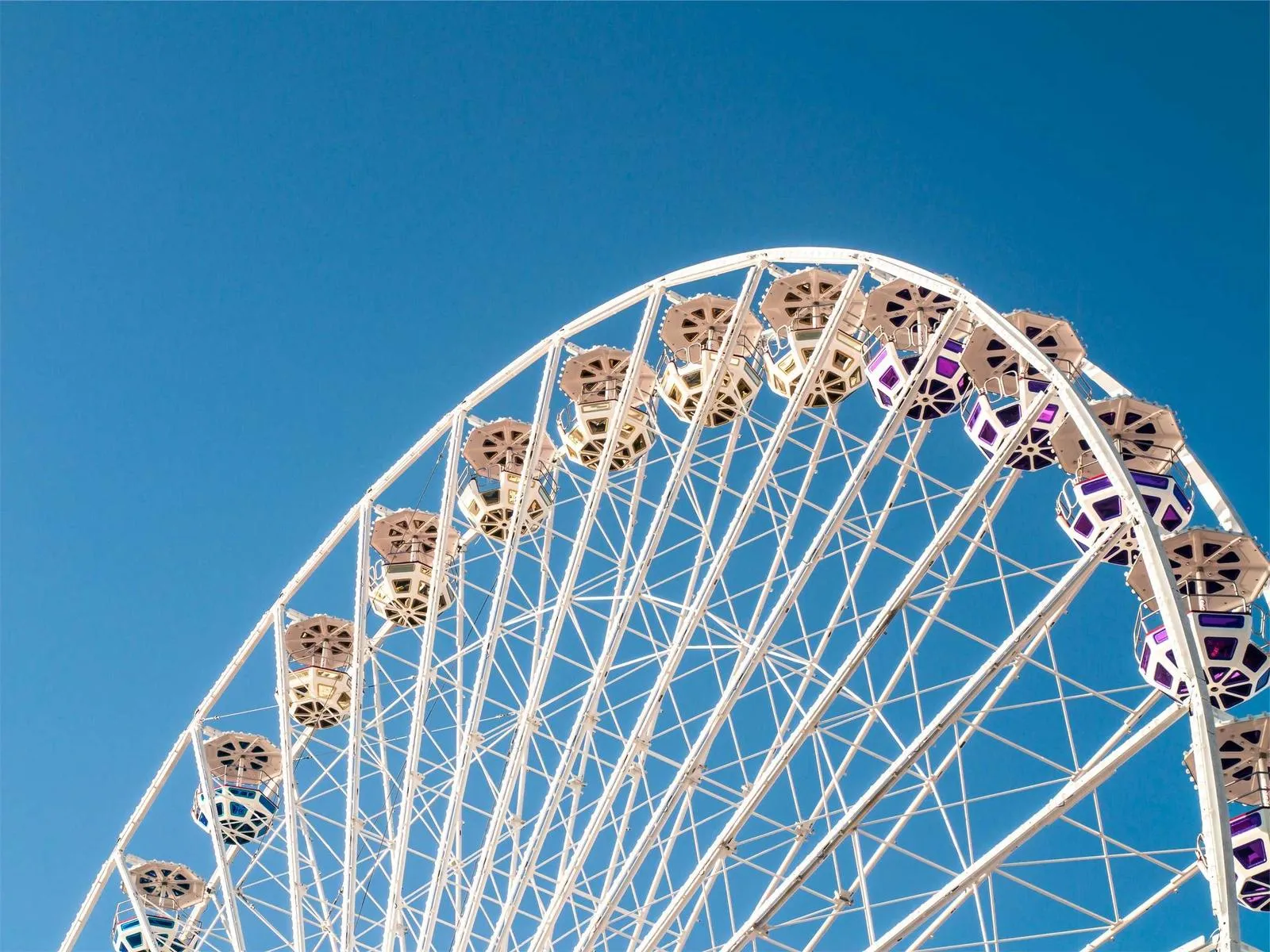 A white Ferris wheel with colorful cabins against a clear blue sky